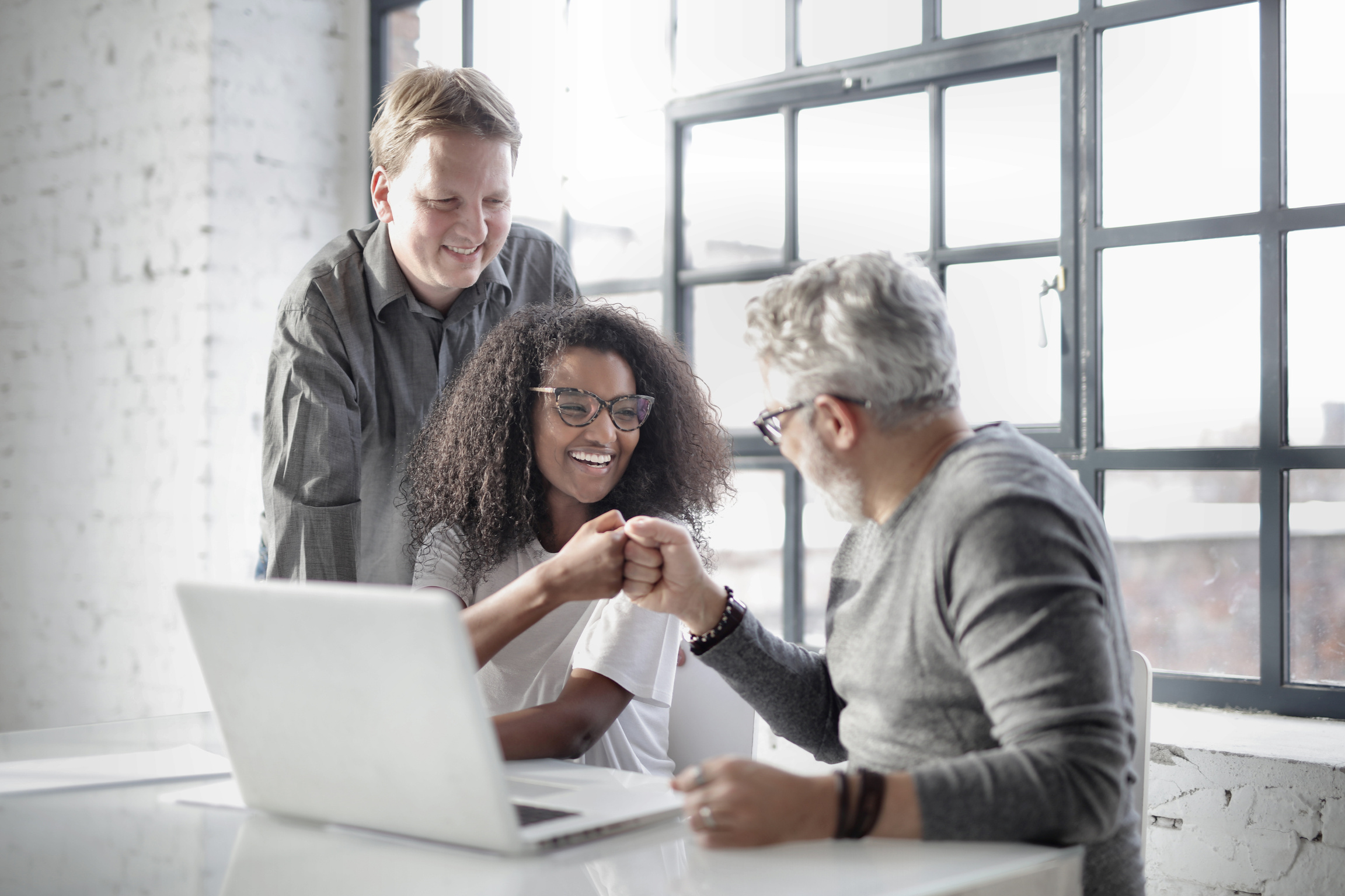 Excited diverse managers achieving success during work on laptop in creative meeting room